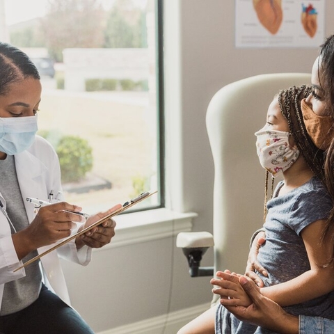 a Black doctor talking with a Black woman and a female Black child